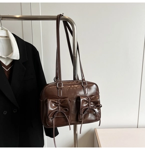 Detail of dark brown glossy shoulder bag featuring twin front pockets and bow accents