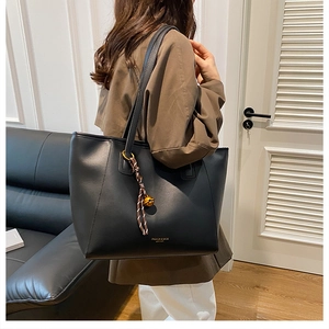 Dettaglio della borsa tote in pelle nera con ciondolo dorato e incisione fashion