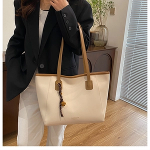 Dettaglio di una grande borsa tote crema con spalline marroni e ciondolo intrecciato elegante