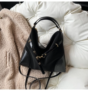 Detailed view of black large capacity tote bag with gold metal accents on white cushion