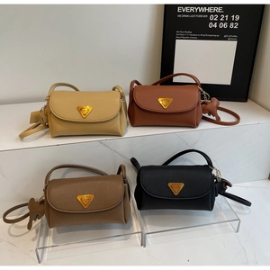 Close-up of four colors of pebbled leather crossbody bags with metal logo and doll charms