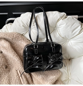 Close-up of black patent leather handbag featuring dual pockets with decorative bows