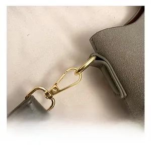 Detailed macro view of the premium gold metal hook on a gray leather bucket bag strap