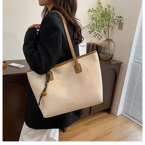 Dettaglio della borsa tote beige in finta pelle con manici marroni e ciondolo a nastro