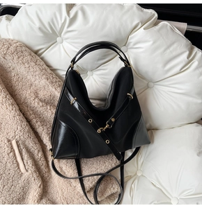 Detail of black nylon and patent leather bag with gold buckle on a soft white cushion