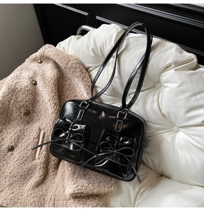 Detail of glossy black leather handbag with 3D bows and decorative white stitching