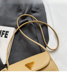 Detail of light yellow lychee grain leather crossbody bag with golden triangle hardware