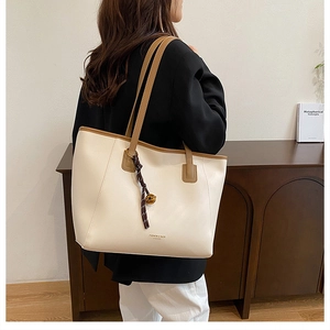 Dettaglio della borsa tote in pelle crema con tracolla marrone e ciondolo a nappa