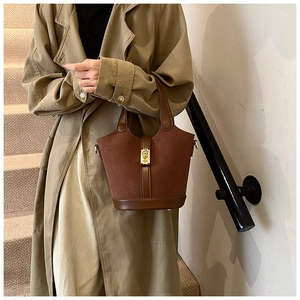 Detail of brown suede bucket bag featuring leather trim and a golden square buckle