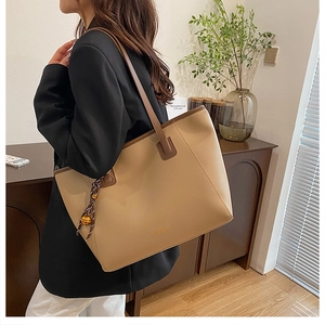 Dettaglio di una borsa tote in pelle beige con manici marroni e ciondolo a campanella