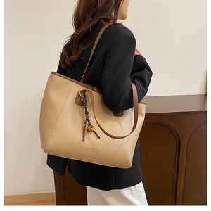 Dettaglio della borsa tote beige con manici marroni e ciondolo intrecciato