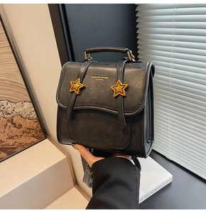 Detail of black retro leather bag with golden star buckles and top handle held by hand