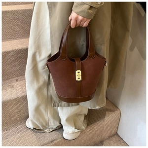 Close-up of vintage brown suede bucket bag featuring golden H-shaped clasp and leather handle