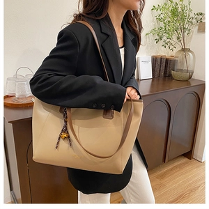 Dettaglio della borsa tote beige con manici marroni e sciarpa di seta su modella