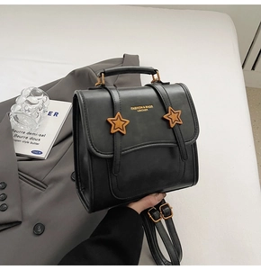 Close-up of black leather bag with gold star accents on a grey blazer background