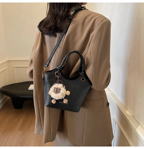 Detail of black matte leather bucket bag with cute beige sheep plush pendant charm