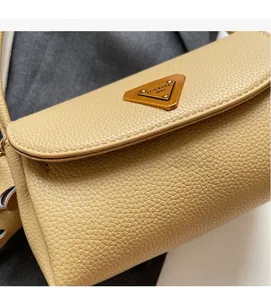 Detailed close-up of beige lychee grain leather texture and metallic logo plaque on the bag