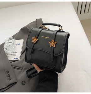 Detail of black leather handbag with two yellow star ornaments and fashion branding