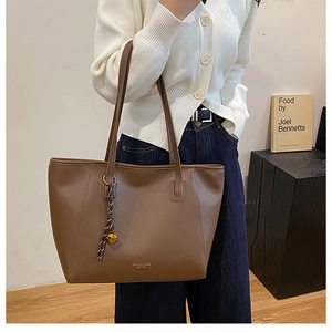 Dettaglio di una borsa tote grande marrone scuro con ciondolo a campana dorata e cuciture