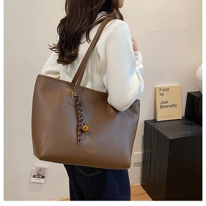 Dettaglio di una borsa tote in pelle marrone con ciondolo dorato e tracolla sottile