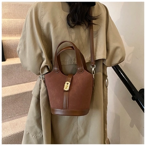 Model styling a tan vintage bucket bag with matte suede texture and golden metal clasp