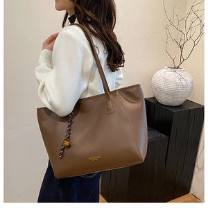 Dettaglio della borsa tote grande in pelle marrone con pendente dorato e nappa decorativa