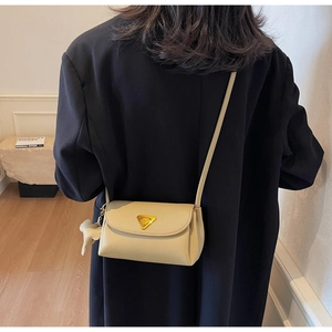 Detail of cream crossbody bag with gold triangular logo and leather bow charm