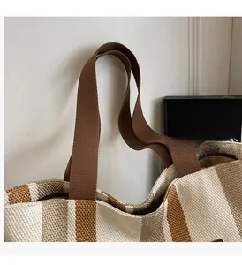 Detail of knitted stripe tote bag showing reinforced brown handles and soft canvas texture