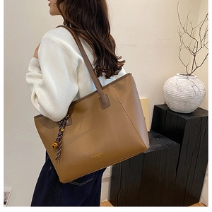 Dettaglio della borsa tote in pelle PU color marrone con nodo intrecciato e campanellino