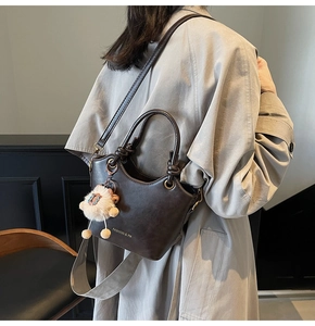 Detail of dark brown bucket bag with plush alpaca charm and wide shoulder strap
