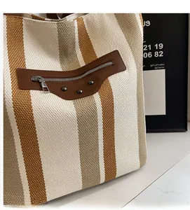 Detail of striped knitted tote bag showing fabric texture and brown leather patch with rivets