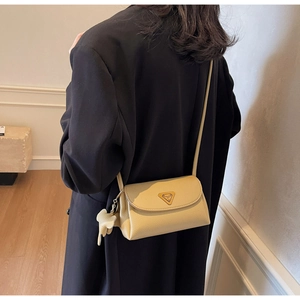 Detail of beige pebbled leather crossbody bag featuring an elephant charm and metal logo