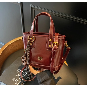 Detail of dark red bucket bag with gold hardware and heart charm on a wooden chair