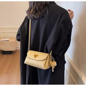Detail of beige litchi leather bag featuring a gold triangle emblem and elephant charm