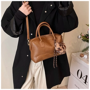 Détail d'un sac oreiller en cuir marron avec pompon léopard et breloque tressée