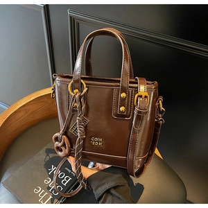 Detail of dark brown tote bag with glossy oil wax texture and pretzel charm hanging on handle