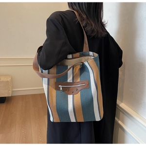 Side view of a striped canvas tote bag with brown straps and leather zip detail