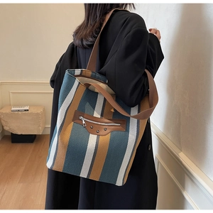 Detail of canvas tote bag with blue and yellow stripes and brown leather zip pocket