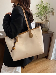 Grande borsa tote beige con manici marroni e ciondolo alla moda indossata da modella