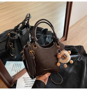 Detail view of a dark brown bucket bag with a plush lion pendant and dual handles