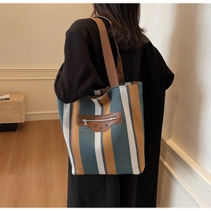 Detail of canvas tote bag with teal and yellow stripes, leather pocket and metal rivets