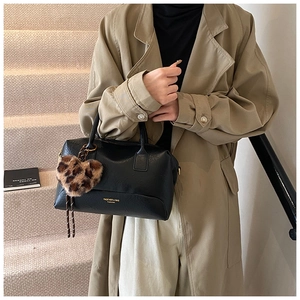 Sac polochon noir porté avec un trench kaki et un charm coeur à imprimé léopard