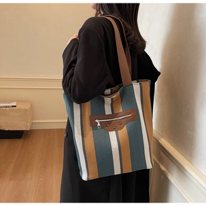 Detail of striped canvas tote with brown leather patch and signature metal rivets