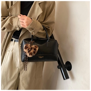 Détail d'un sac oreiller en cuir noir avec breloque cœur léopard sur un trench-coat chic