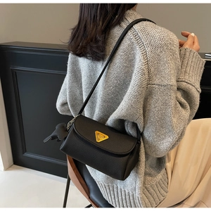 Detail of black lychee grain shoulder bag with gold logo and dog-shaped pendant