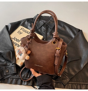 Detailed view of coffee brown bucket bag with plush sheep charm on vintage books