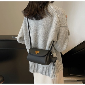Detail of black pebbled leather crossbody bag with golden triangle buckle and elephant charm