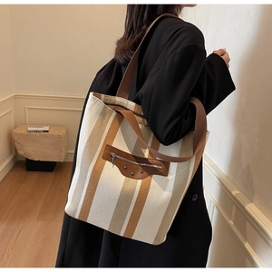 Detailed view of a striped canvas tote bag with front zipper pocket and wide fabric strap