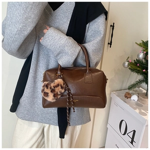 Détail du sac polochon en cuir marron foncé avec breloque cœur léopard et logo doré
