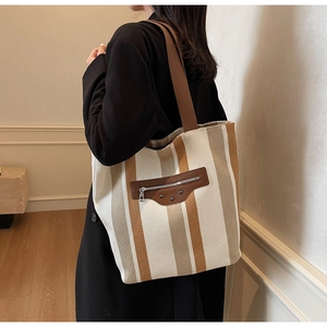 Close-up of striped canvas tote bag featuring leather zipper pocket and metal rivets
